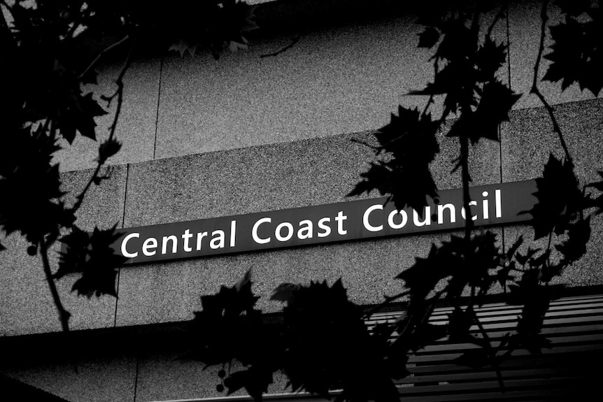 A black and white photo of the Central Coast Council sign with leaves blocking parts of it