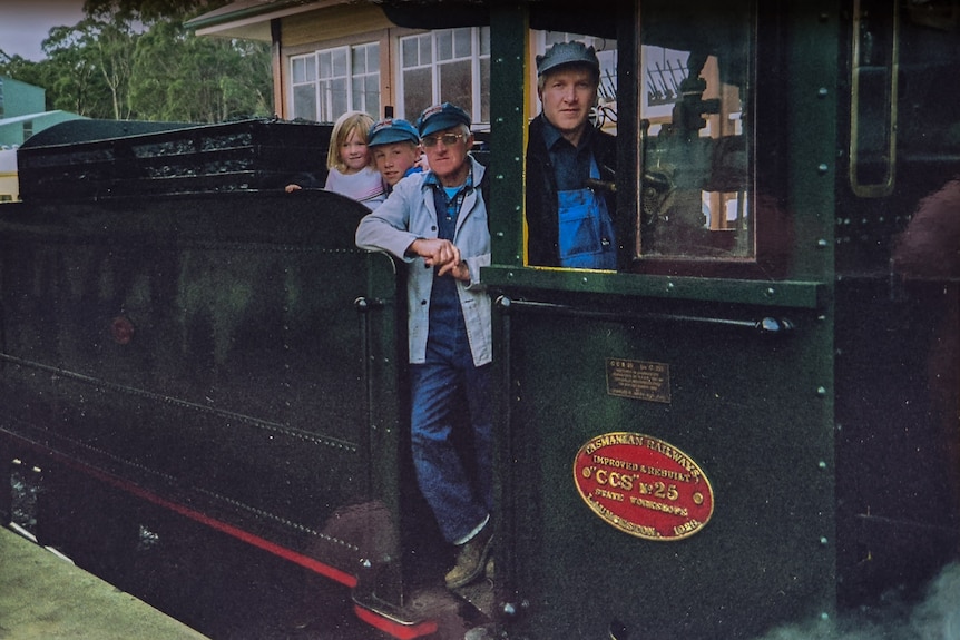 Ageing family photo of three generations of a family posing on a steam train at the station.
