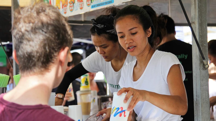 A photo of a juice vendor at a Darwin market handing a cup to a customer.