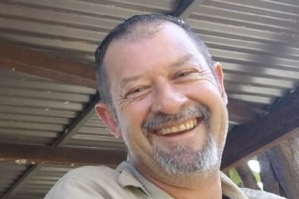A man with a goatee beard smiling and wearing a khaki shirt.