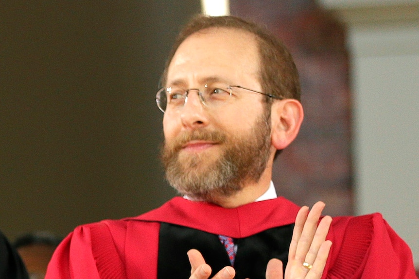 A man looks into the distance wearing a red gown and glasses.