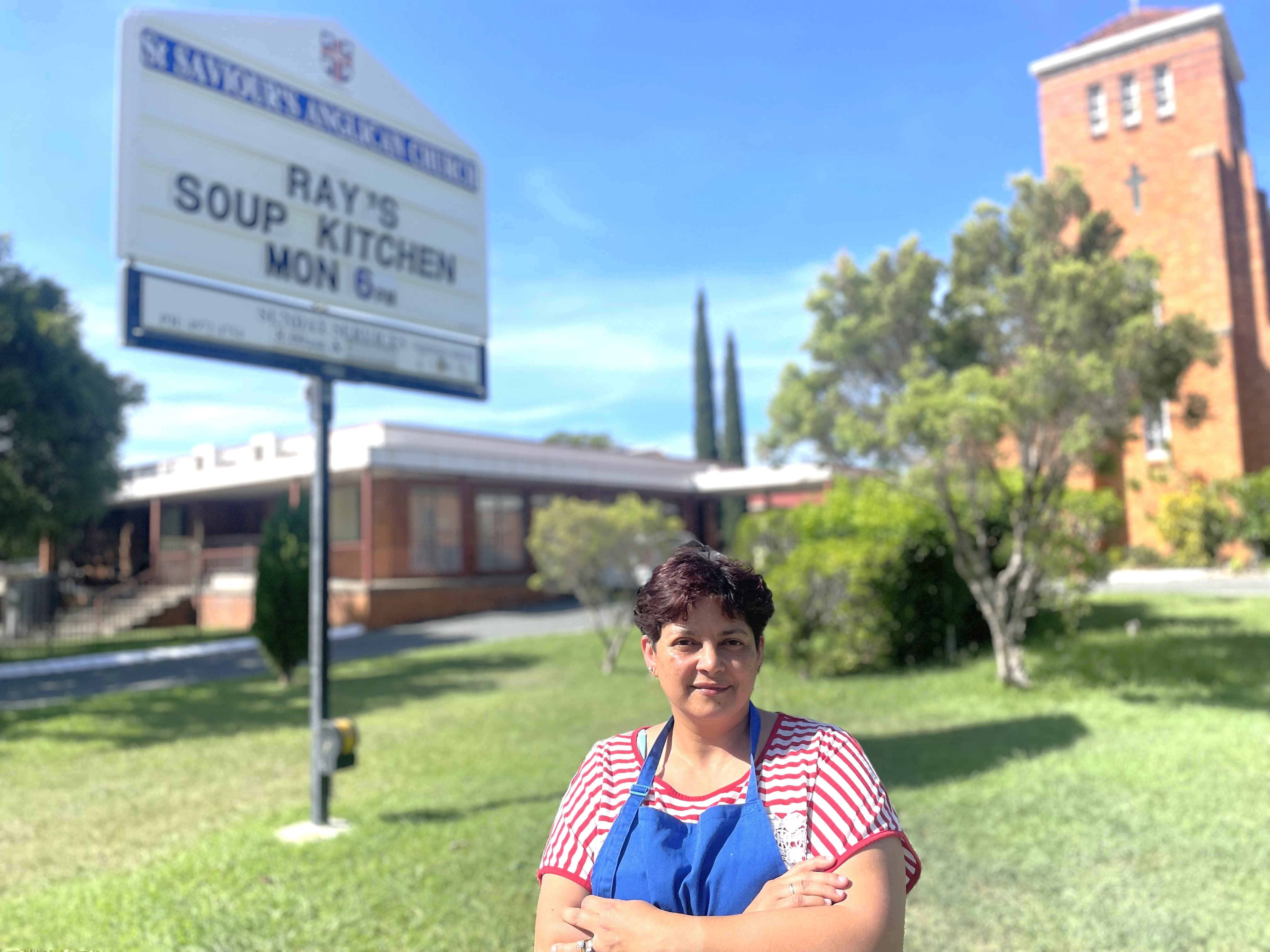 Woman smiles at camera with soup kitchen sign behind her