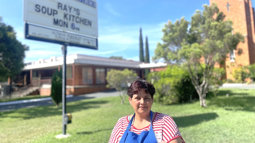 Woman smiles at camera with soup kitchen sign behind her