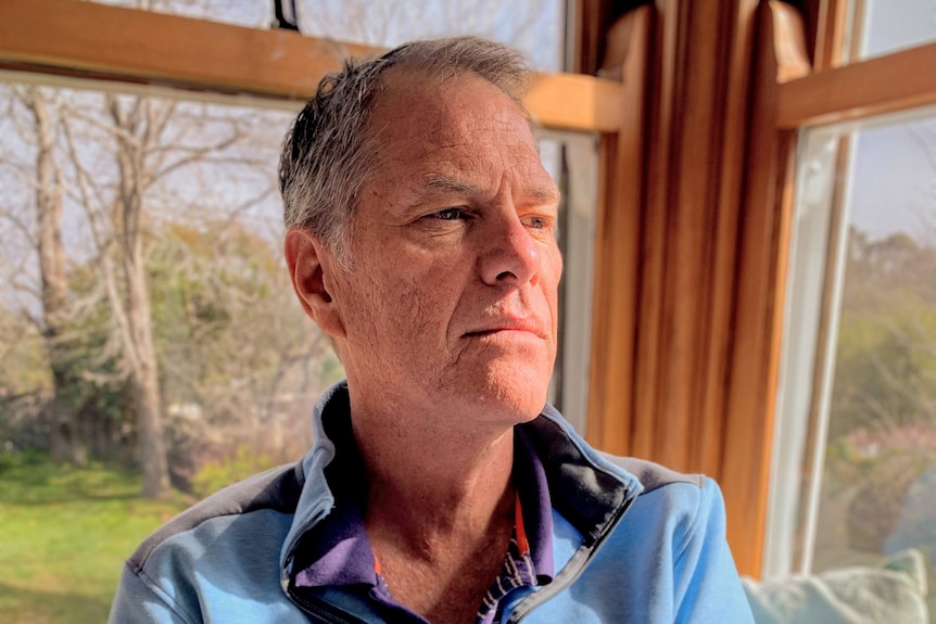 Man in a light blue jumper holding a cup.