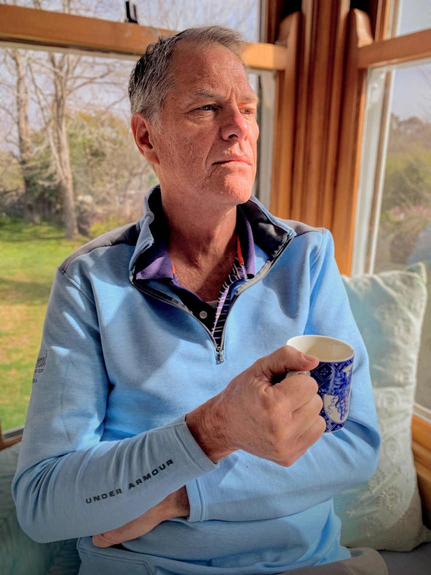 Man in a light blue jumper holding a cup.