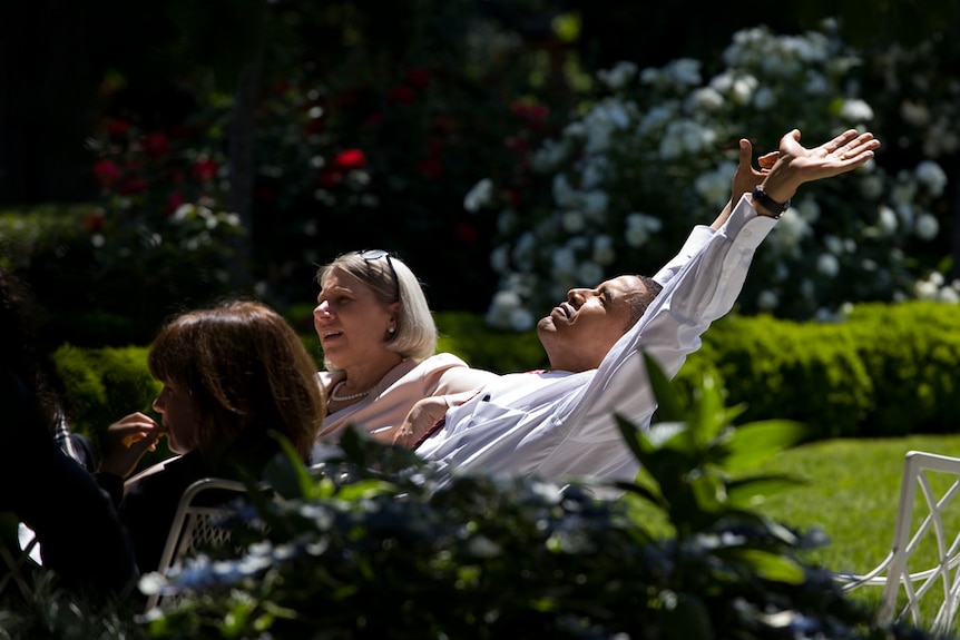 Barack Obama stretches his arms in the sun during an outdoor meeting with his advisors