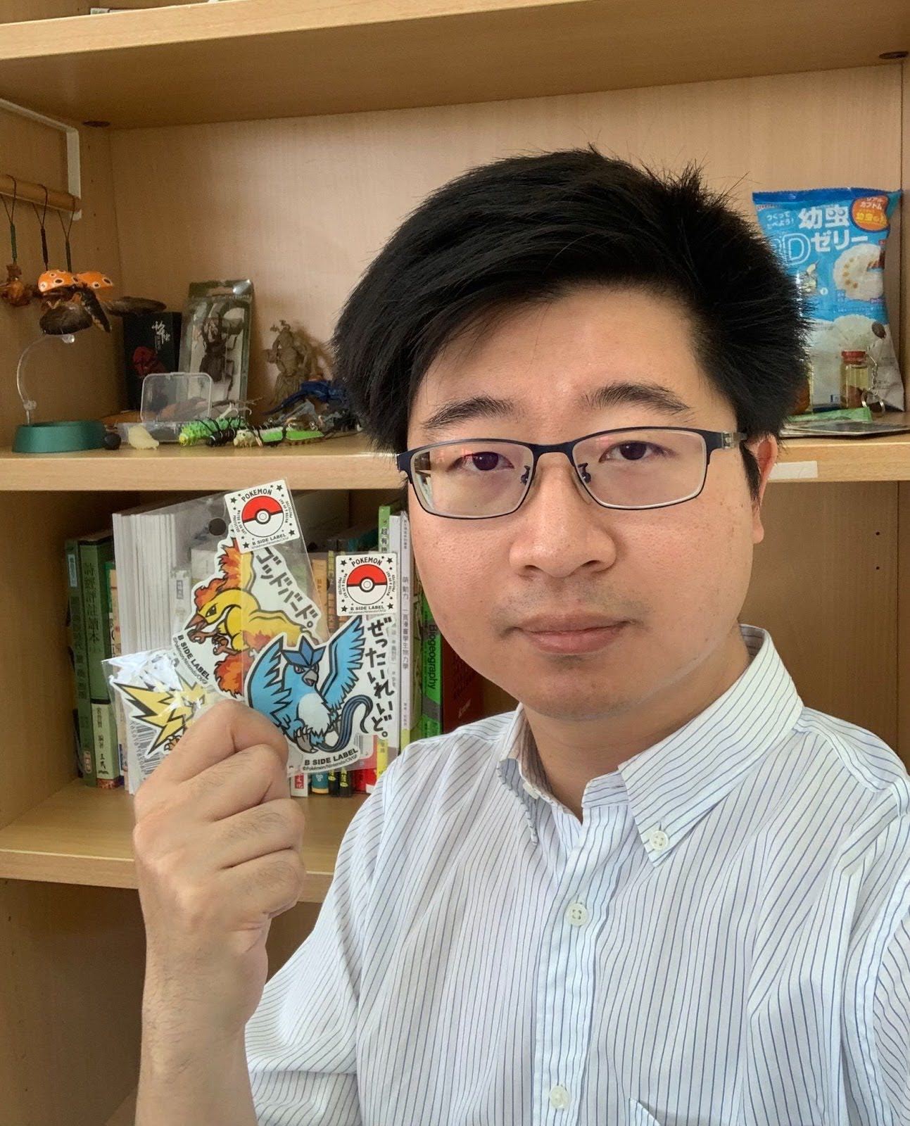 A man in glasses holds up laminated pokemon cut outs