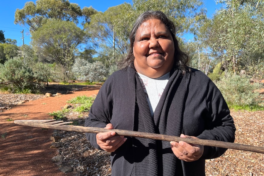 A woman standing outside and holding an Aboriginal spear.