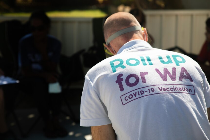 A man sits in a driveway, wearing a shirt reading Roll Up for WA.