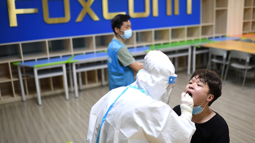 一名身穿防护服的医护人员在富士康工厂收集一名工人的棉签样本，用于核酸检测。