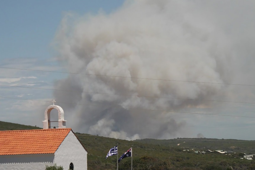 A thick cloud of smoke from a bushfire fills the sky above hills and a church.
