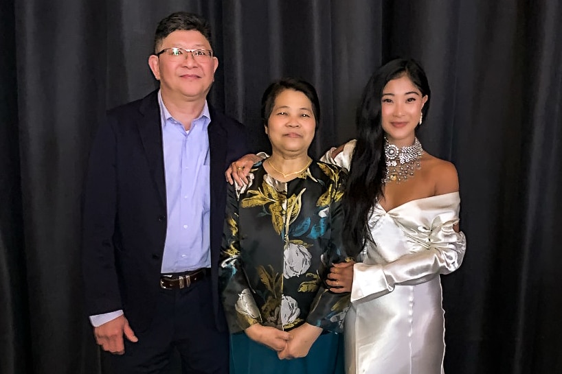 A woman in white dress smiling next to her mother and father. 