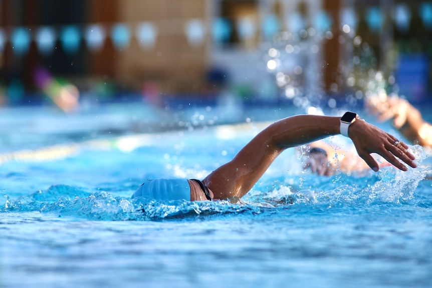A swimmer does freestyle in a swimming pool at Bold Park. She wears a swimming cap and goggles.