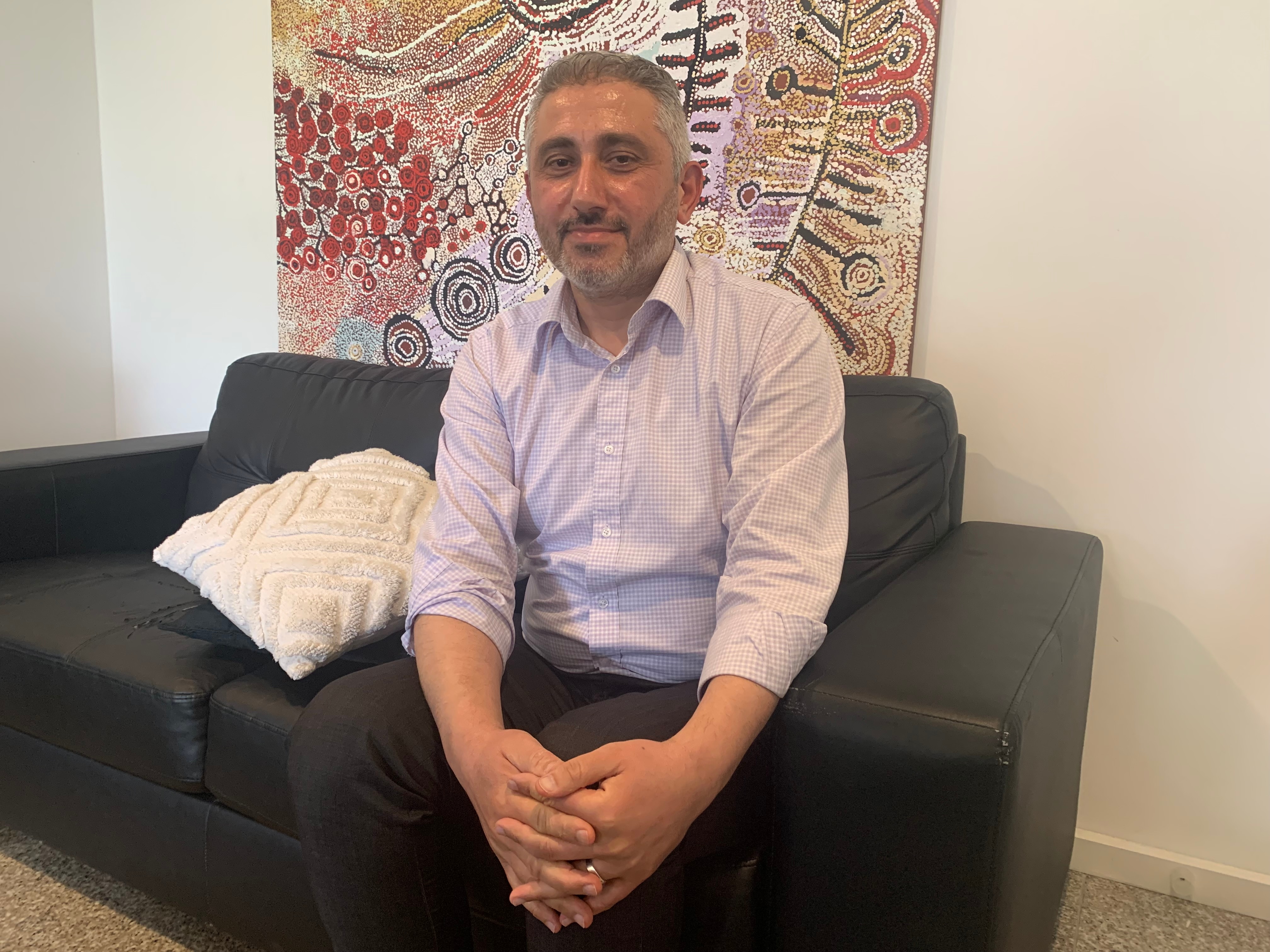 Un hombre sentado en un sofá frente a una pintura de puntos aborigen