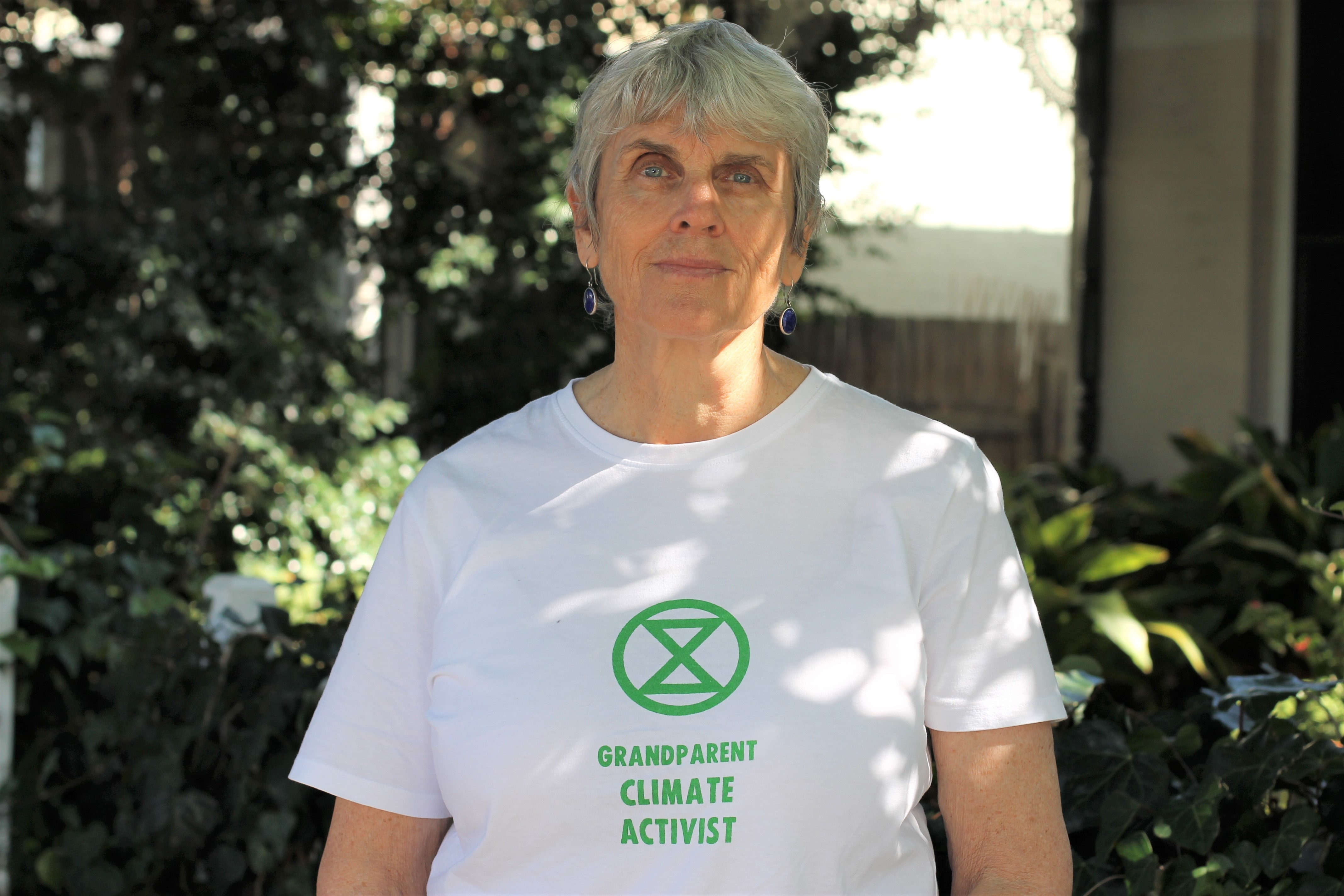 Heath Greville standing in front of a garden with a white t-shirt on with words "Grandparent climate activist"