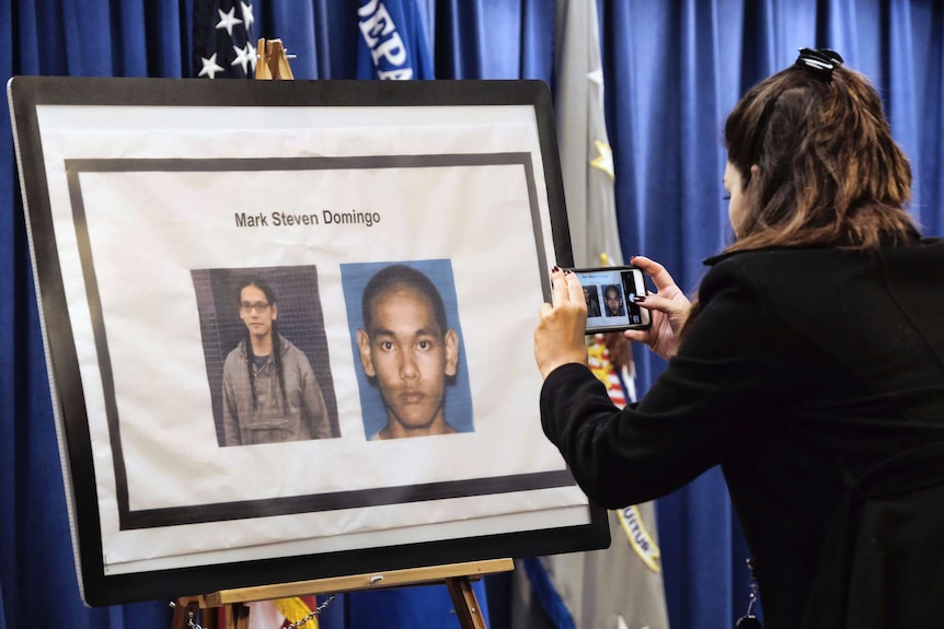 A woman takes a phone photo of a board displaying images of terror suspect Mark Domingo.