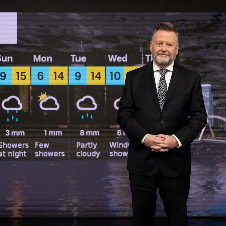 Paul Higgins standing in front of a large screen with Melbourne's weekly weather forecast. 