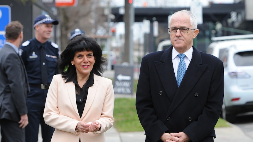 Julia Banks, who is smiling, and Malcolm Turnbull, who looks serious, walk down the street.