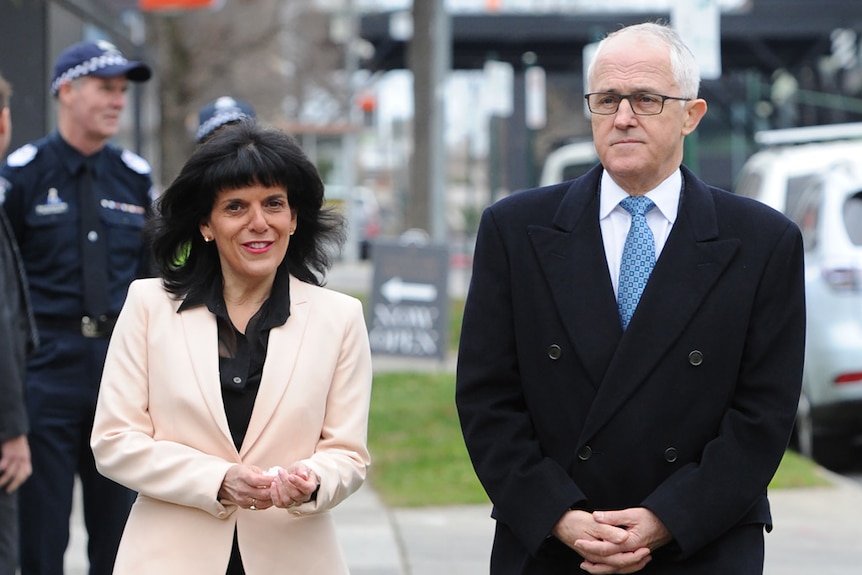 Julia Banks, who is smiling, and Malcolm Turnbull, who looks serious, walk down the street.