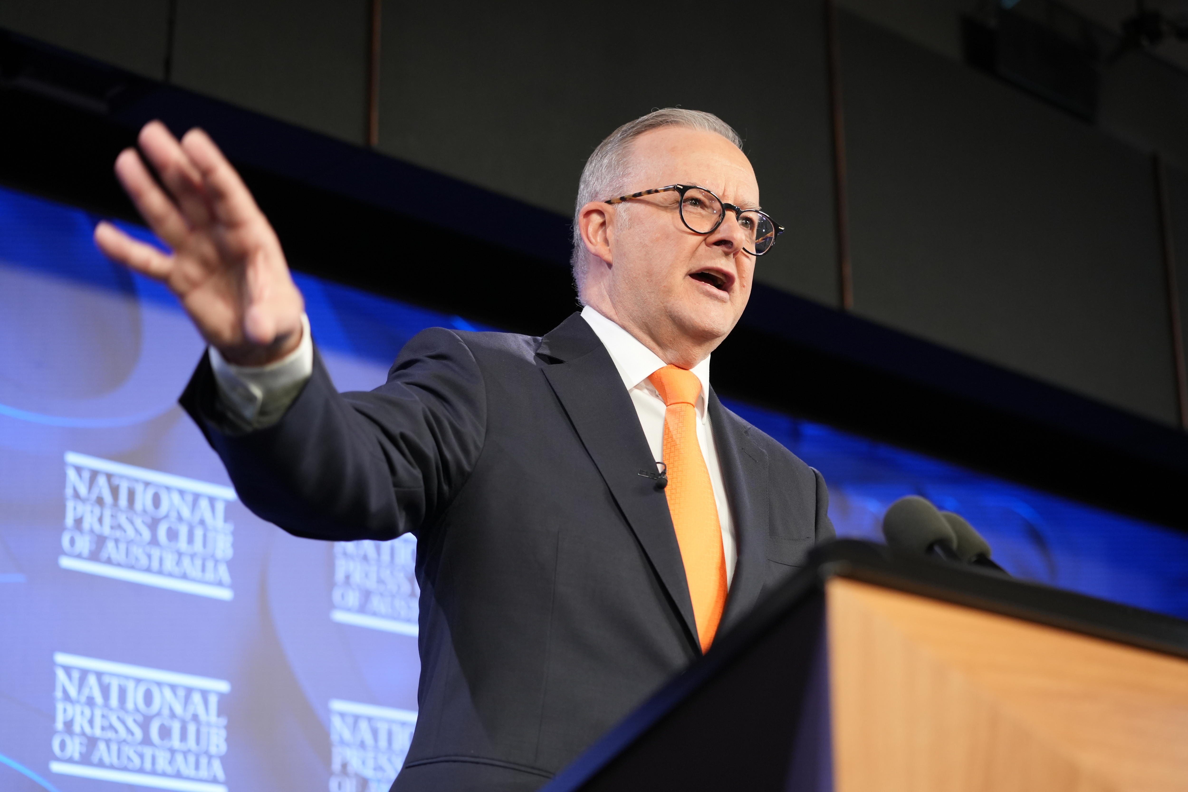 A man in an orange tie and a black and white suit stands at a podium.