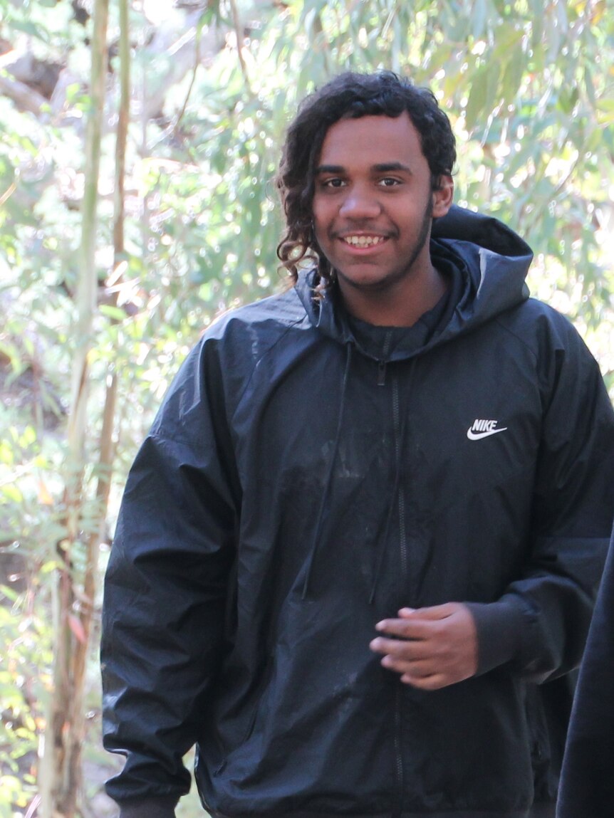 A young Indigenous man wearing a black jacket, smiling.