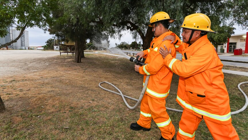 Two Filipino members of the Pyramid Hill CFA practice with  the fire hose.