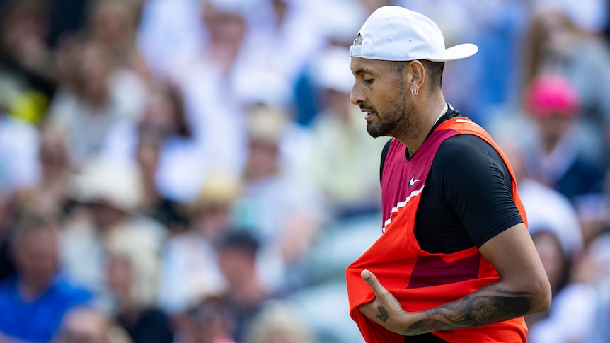 Australia's Nick Kyrgios looks down on court as he holds his tennis singlet during a match.