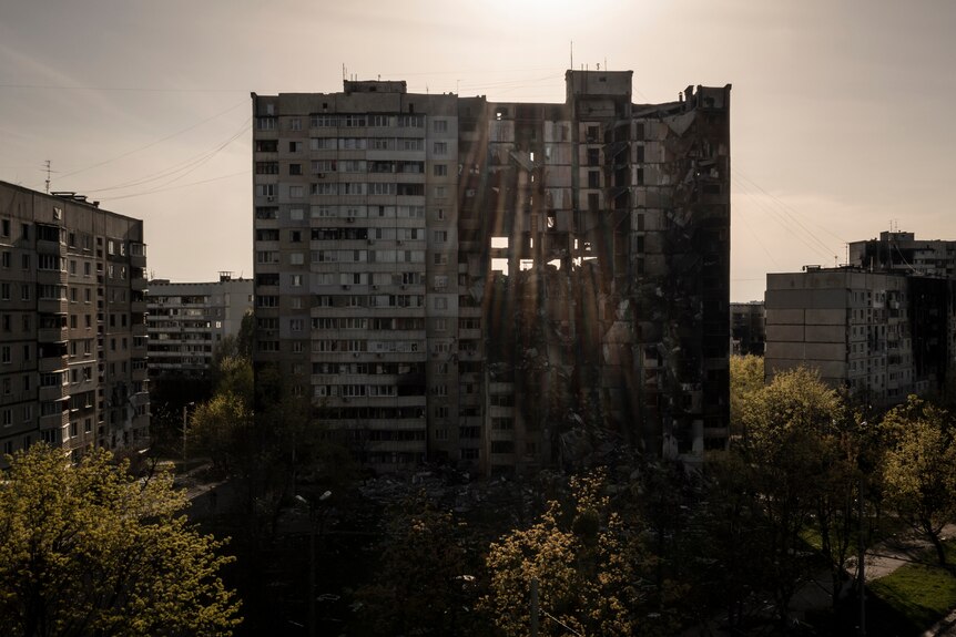 A wide exterior photo of a large residential building damaged by military shelling.