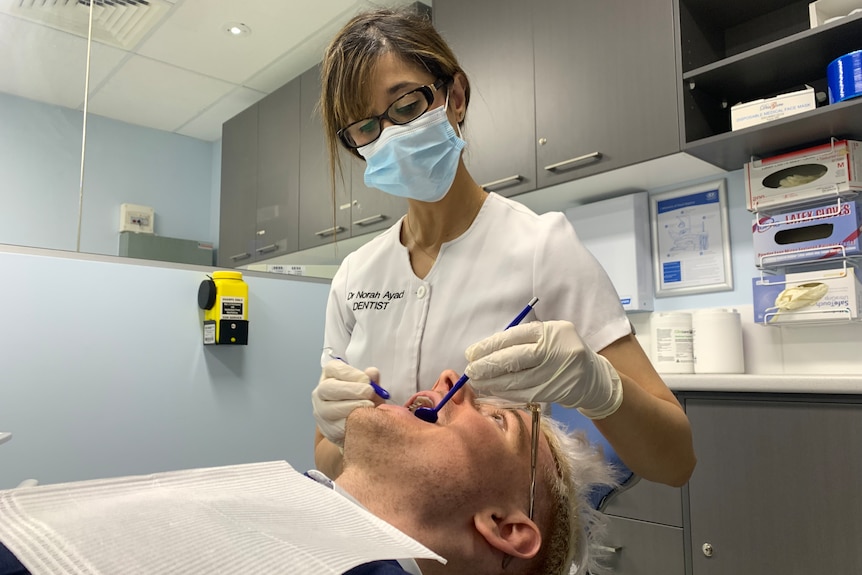 La Dra. Norah Ayad trabajando en la boca abierta de un paciente en su clínica de odontología.
