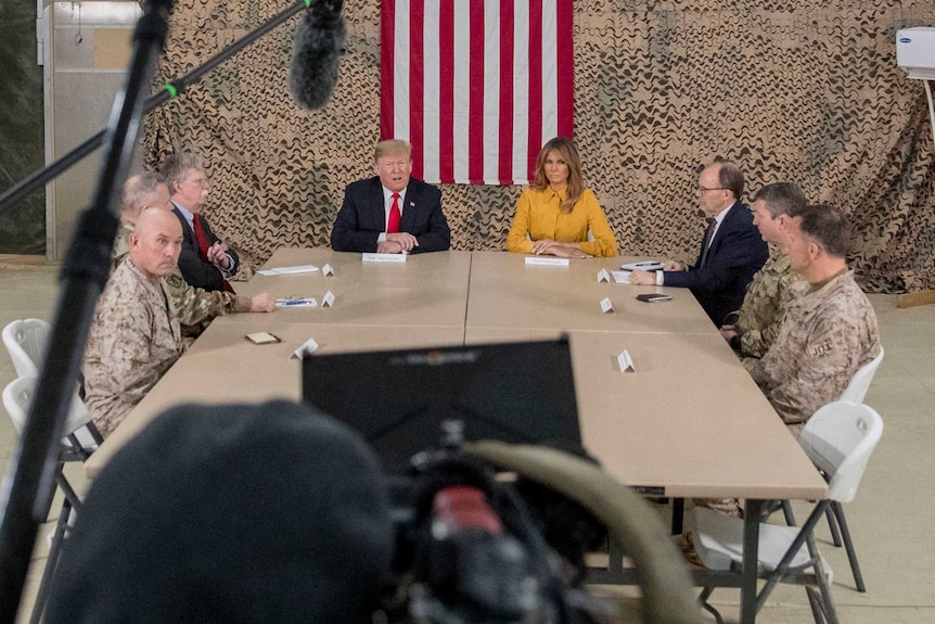 Donald Trump, his wife Melania and government and military advisers sit around a table in a military tent at an airbase in Iraq.