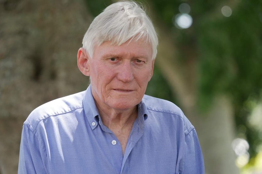 Man with grey hair and blue button up shirt looks into camera.