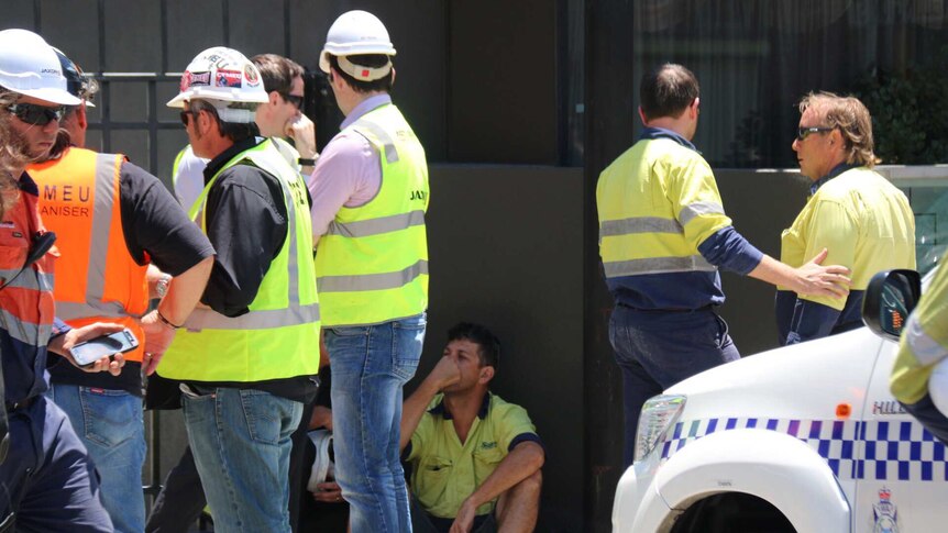 Workers stand in a group talking outside an East Perth construction site.