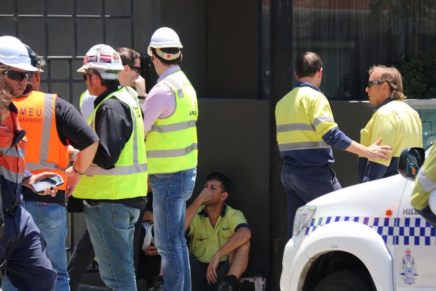 Workers stand in a group talking outside an East Perth construction site.