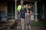Kristy and Scott Aitken and their two daughters and dog smiles as they stand in front of their home.