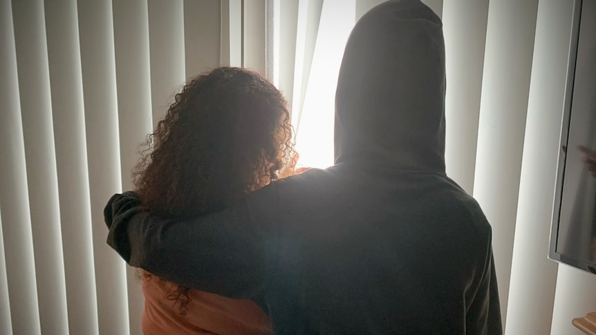 picture of a woman from behind holding a dog, standing next to the blinds