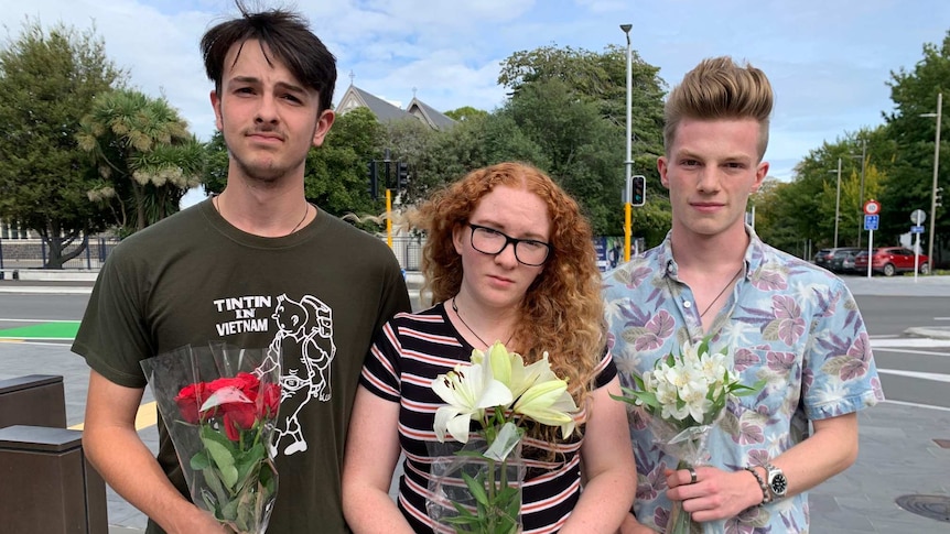 Three people stand holding flowers.