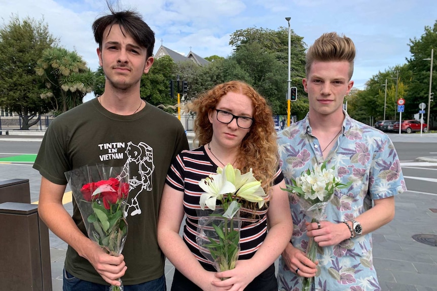 Three people stand holding flowers.