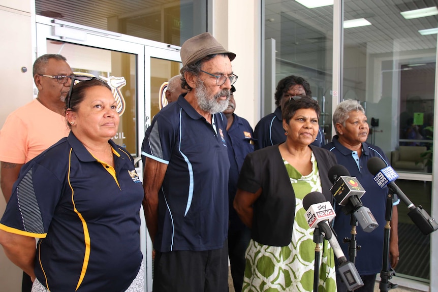 A group of people stand before microphones at a press conference.