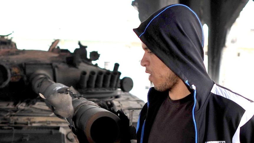 A Libyan rebel walks past a tank belonging to Moamar Gaddafi forces that was destroyed