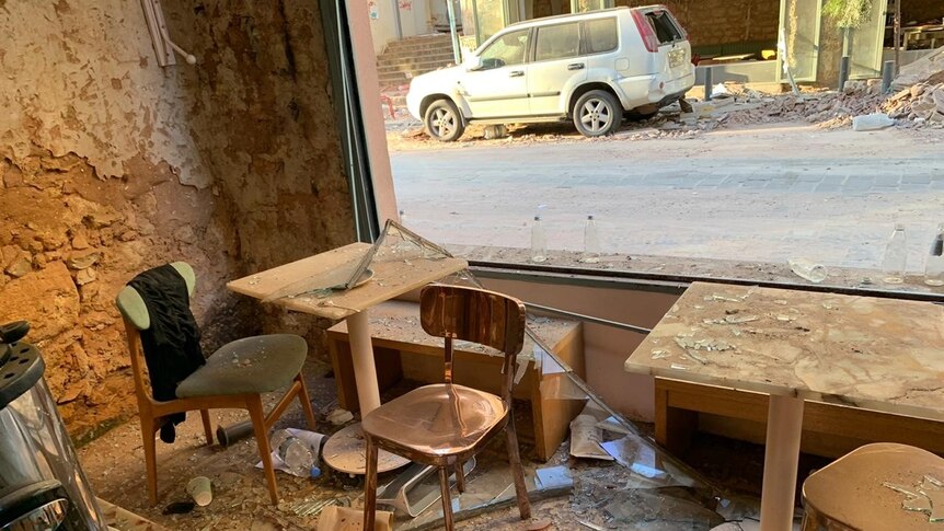 The inside of a damaged coffee shop with windows shattered, and rust and rubble surrounding a table and chairs.