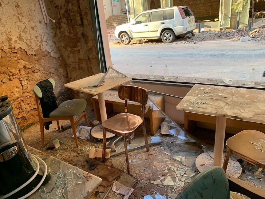 The inside of a damaged coffee shop with windows shattered, and rust and rubble surrounding a table and chairs.