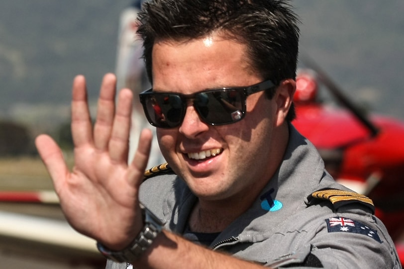 Ryan Campbell, wearing sunglasses, waves as he stands next to a plane.