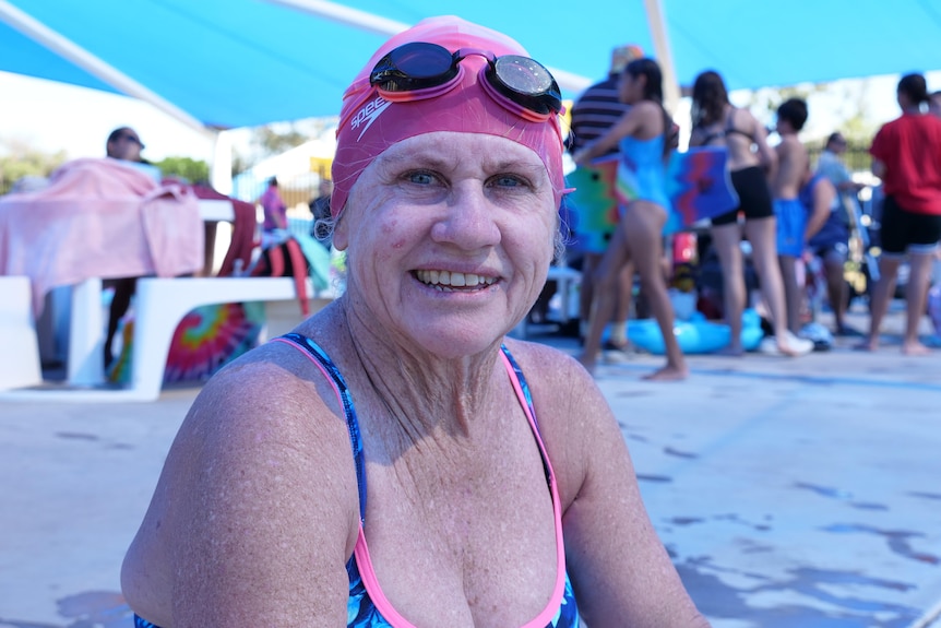 Woman with swimming cap and goggles, smiling out of the water