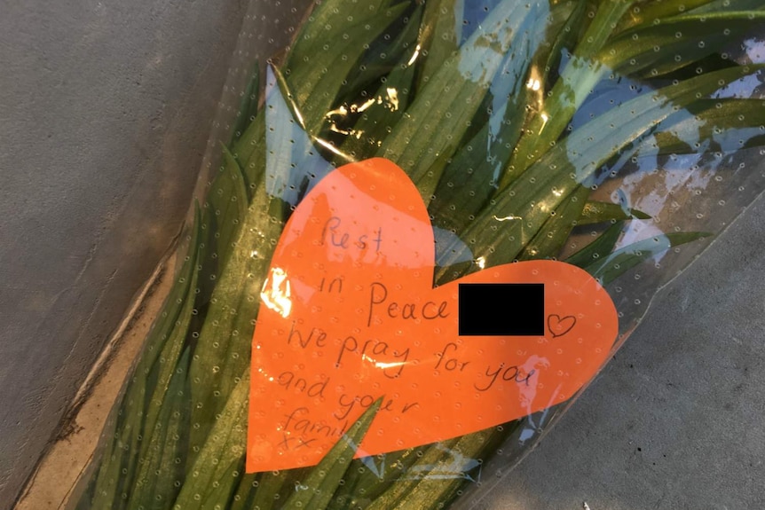 Close up of bunch of flowers with card saying "rest in peace, we pray for you and your family"