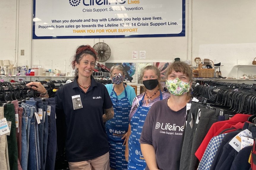 Four women standing in front of clothes racks in a second hand store