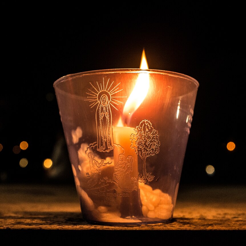 A lit glass candle featuring Virgin Mary sits on a table