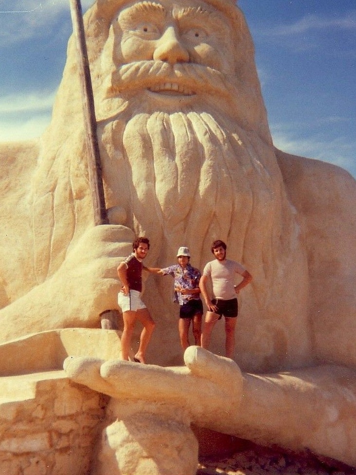 Three people stand in the hand of a giant statue of King Neptune.