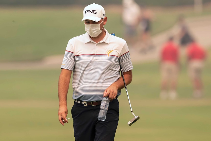 A male golfer wearing a face mask walks along the fairway at the Australian Open