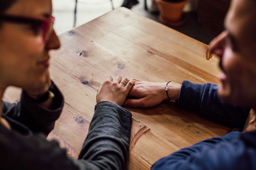 Man and woman chat at a table while holding hands