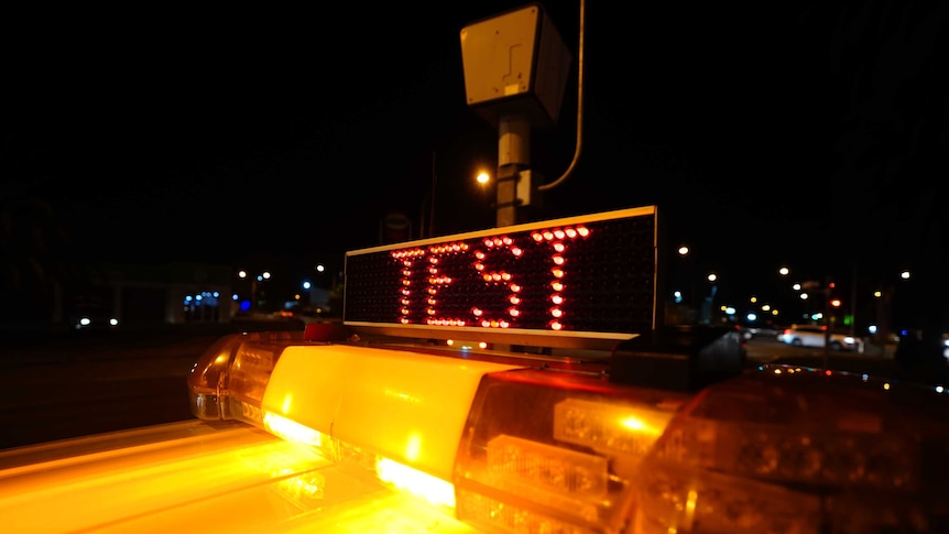 An LED sign that says 'test' sits on top of a police car in front of a red light camera